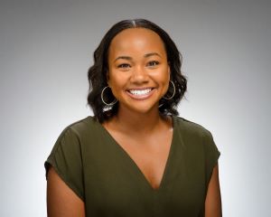 Kerri-Anne has short black hair and is smiling while wearing a green shirt