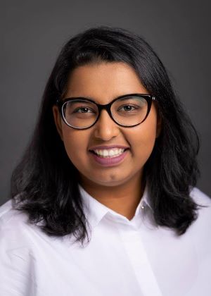 Image of Huda wearing black glasses and a white top, smiling