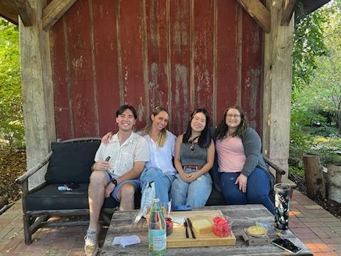 Irene, Veronika, Connor, and Megan sit on a couch outside in front of a wooden building