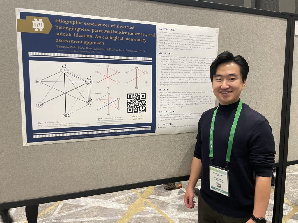 Grad student stands in front of his research poster smiling, wearing a black shirt