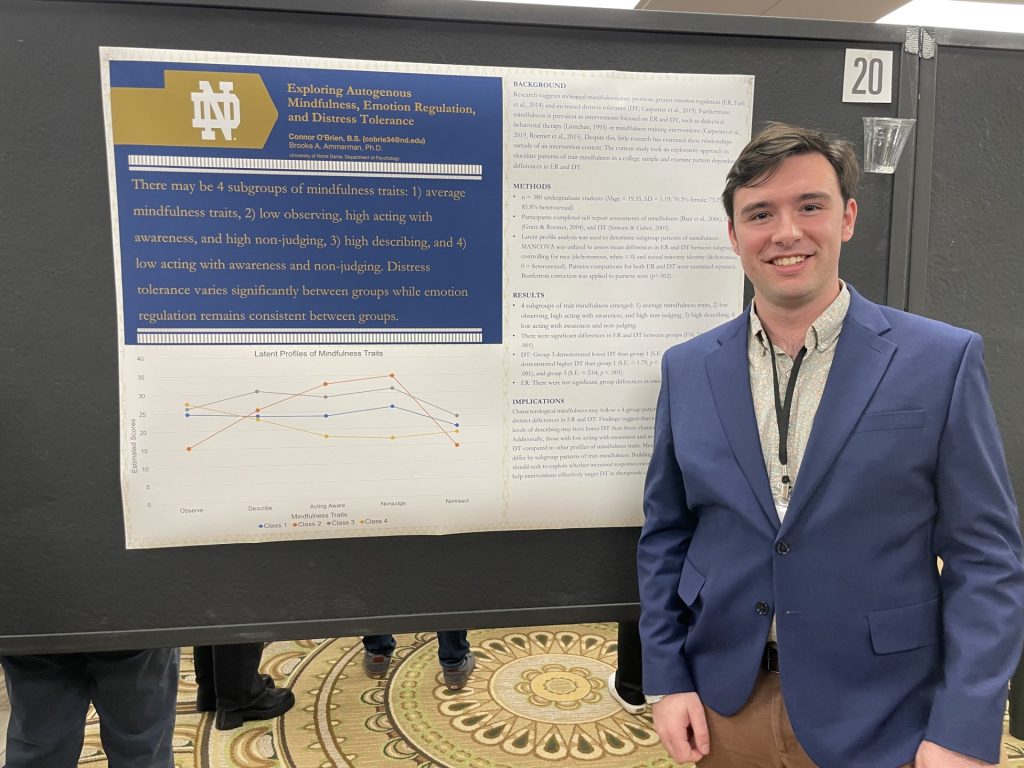 Connor stands smiling in a blue suit in front of his research poster