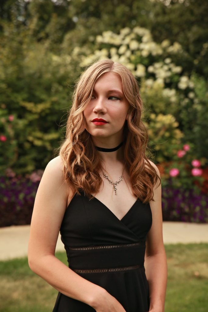 Isabelle has long, light brown hair and is wearing a black dress outside