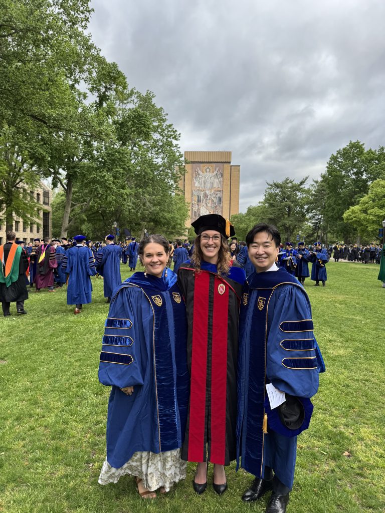 Caitlyn, Brooke, and Yeonsoo (left to right) stand in their graduation regalia smiling outside
