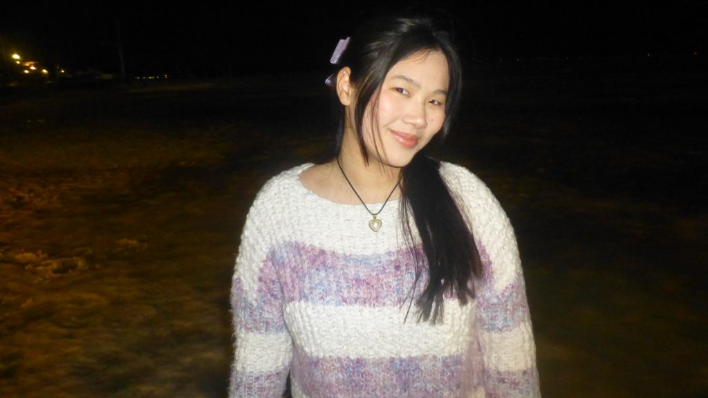 Jenna has long black hair and is smiling wearing a purple and white sweater 