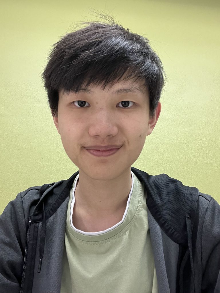 Carl has short black hair, smiling and wearing a light green shirt and a black jacket