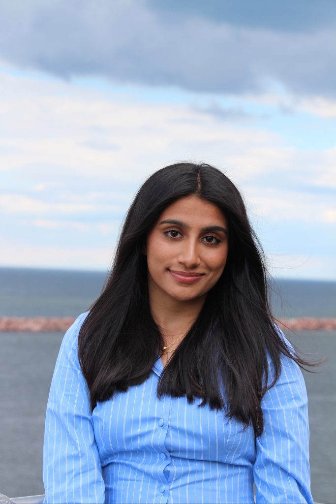 Iman has medium-length black hair and is smiling outside wearing a light blue shirt