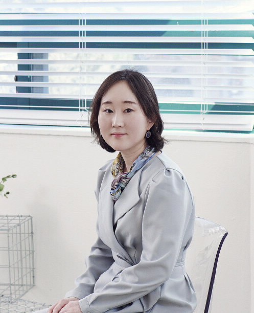 Minkyung is wearing a light gray suit with has shoulder length hair. 