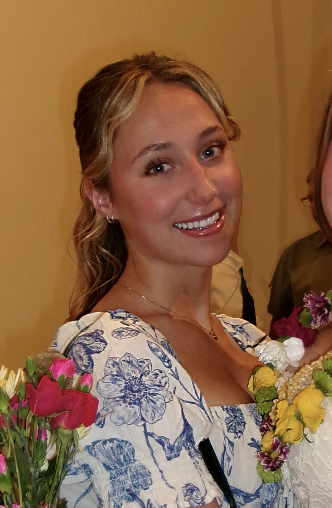 Tess is smiling and wearing a floral dress. 